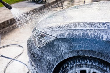 Sabunlu köpükle kaplı bir araç bir oto yıkama tesisinde temizleniyor. Su ve köpük bir araya gelince, araba yüzeyi parlıyor, iyice yıkanmasını sağlıyor.