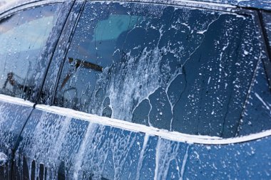 Güneşli bir öğleden sonra, yerel bir oto yıkamada bir araba sabun köpüğüyle kaplanır. Güneş ışığı kabarcıklardan yansıyarak ışıl ışıl bir etki yaratır. self-servis araba yıkama