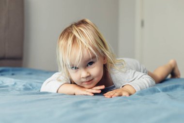 Güzel sarışın küçük bir kız evde bir yatakta şakacı bir şekilde yatıyor, etrafını sabah ışığı sarmışken dikkatle bakıyor. Samimi ortam Childs 'ın masumiyetini ve cazibesini vurguluyor..