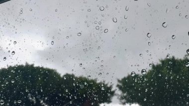 Arabanın yan camında yağmur damlaları var. Yoldan geçen bir arabanın içinden görüntü. Bulanık arka plan. Yağmurda Araba Kullanmak. Otomatikten sağanak yağmurun görüntüsü. # Yaz gününde yağmur ve gri bulutlar #