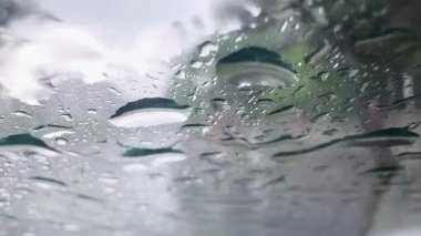 Araba camına yağmur damlaları. Türkiye 'de yağmurlu bir yaz günü, Antalya. Farklı projeler için kamera arkası. Arka planda arabaların farları ve şehir görünür..