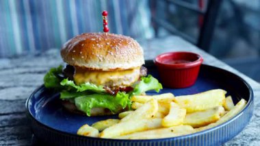 Mavi tabakta kızarmış patatesli bir Amerikan hamburgeri. Sağlıksız gıda konsepti. Kafede ya da restoranda çizburger ve patates kızartması, fast food. 