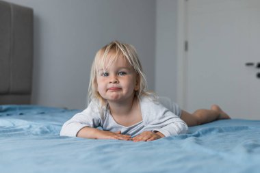 Açık bluzlu neşeli sarışın bir kız evdeki mavi bir yatak örtüsünün üzerinde rahatça yatıyor. Karnı üzerinde dinlenirken, huzurlu bir keşfe girişerek, bir anlık rahatlamanın tadını çıkarıyor..