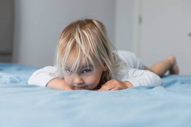 Sarışın, yeni yürümeye başlayan bir kız evdeki yumuşak bir yatakta kameraya merakla bakıyor. Neşeli ifadesi çocukluk ruhunu samimi bir ortamda yakalıyor..