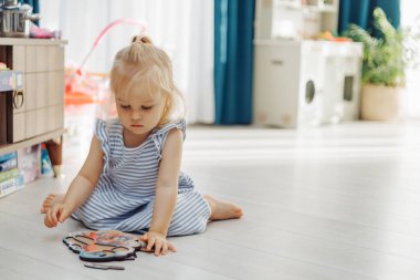 Genç kız içeride yerde sessizce otururken renkli bir oyuncağa odaklandı. Oyunda yeteneklerini geliştirmek için tahta çevre dostu oyuncaklar.