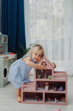 Açık renk saçlı küçük bir çocuk, canlı oyuncak evin yanındaki rahat mekanda oyun oynamaktan zevk alıyor..