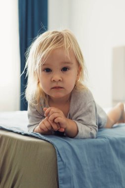 Güzel sarışın küçük bir kız evde bir yatakta şakacı bir şekilde yatıyor, etrafını sabah ışığı sarmışken dikkatle bakıyor. Samimi ortam Childs 'ın masumiyetini ve cazibesini vurguluyor..