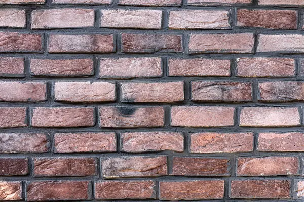 Türlü kırmızı ve kahverengi tuğlalar sergilenen desenli tuğla duvarın yakın plan görüntüsü. Düzenleme, şehir ortamında bulunan pürüzlü yüzeyleri ve farklı renkleri vurgular.