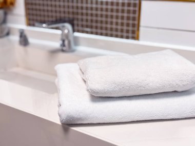 Çağdaş bir banyoda temiz beyaz havlular şık bir tezgahın üzerinde durur. Minimalist tasarım, aydınlık ve temiz atmosferi tamamlayarak, bir sakinlik ve hijyen duygusunu vurguluyor..