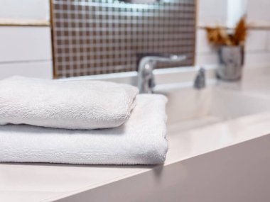 Çağdaş bir banyoda temiz beyaz havlular şık bir tezgahın üzerinde durur. Minimalist tasarım, aydınlık ve temiz atmosferi tamamlayarak, bir sakinlik ve hijyen duygusunu vurguluyor..