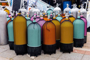 Güneşli bir günde bir dalış mağazasının önünde canlı renklerde çeşitli tüplü dalış tankları sergileniyor. Yaz tatilleri, turizm, geziler ve aktif hobiler konsepti