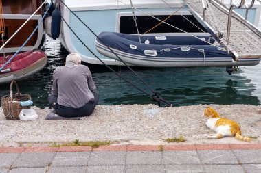  Yaşlı bir balıkçı balık yakalar, deniz kenarındaki huzurun tadını çıkarır yanında dinlenen bir kedi ve bir balığı bekler.