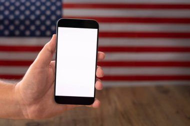 Beyaz ekranlı cep telefonlu erkek eli metin ya da ürün, model, arka plan ABD bayrağı.
