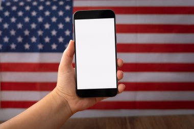 Metin veya ürün için beyaz ekranı olan cep telefonlu bir kadın el, model, arka plan ABD bayrağı.