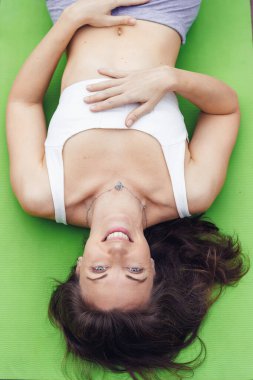 Uzun kahverengi saçlı beyaz bir kadın yeşil yoga minderinde uzanıyor, kulaklık takıyor ve rahat bir şekilde müziğin tadını çıkarıyor..