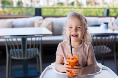 Mutlu gülümseyen kız, kafede havuç suyu içiyor.