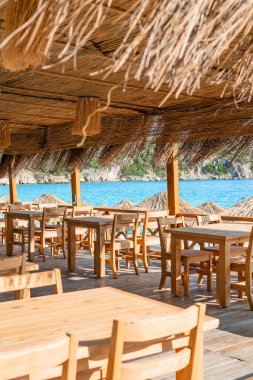 Büyüleyici bir sahil yemek alanı, açık mavi deniz manzarası sağlayan ahşap masalar ve güneş şemsiyeleri içerir..
