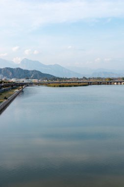 Sakin bir nehir mavi gökyüzünü ve yakındaki dağları yansıtır. Bereketli yeşillik kıyıları çevreleyen, suları aşan bir köprüyle, Antalya şehrinde huzurlu bir manzara yaratıyor.