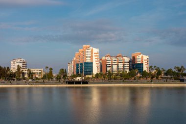 Sakin bir kıyı şeridi günbatımının yumuşak renklerini yansıtır. Sahil şeridi, Antalya şehri manzarası ve rahatlama ve rahatlama için pitoresk bir ortam oluşturan binalar ve palmiye ağaçlarıyla kaplı.