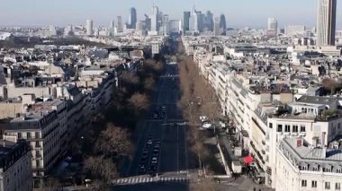 Arka planında modern gökdelenler olan bir şehirde geniş, boş bir caddenin havadan görünüşü. Sahne, şehir mimarisini ve açık gökyüzünü yakalıyor..