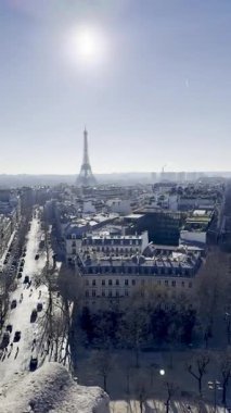 Fransa, Paris - 14.01.2025: Arka planda Eyfel Kulesi olan Paris 'in panoramik görüntüsü. Sahnede açık mavi bir gökyüzü ve şehrin sokaklarını aydınlatan güneş ışığı yer alıyor..