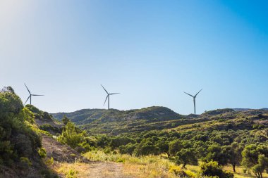 Türkiye 'de açık mavi gökyüzünün altındaki yeşil tepelerde rüzgar türbinleri. Manzara, yenilenebilir enerjiyi ön plana çıkaran yemyeşil bitki örtüsü ve sakin bir çevreye sahiptir..