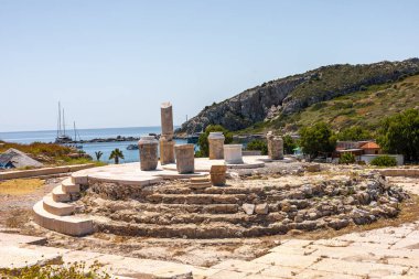 Türkiye 'de deniz manzaralı bir yamaçtaki antik kalıntılar. Taş yapılar ve sütunlar yeşil ve kayalık arazilerle çevrili olarak görülebilir..