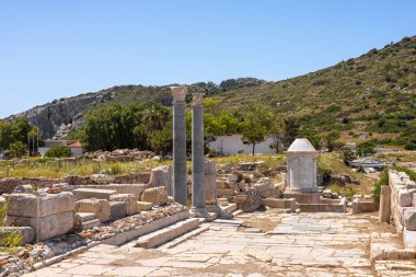 Türkiye 'de taş sütunları ve küçük bir anıtı olan antik kalıntılar. Açık mavi gökyüzünün altında yemyeşil tepeler.