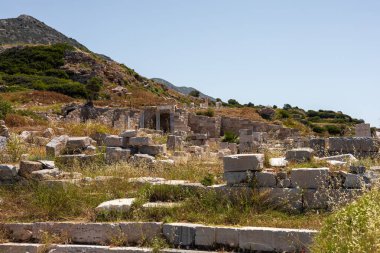 Yeşil tepeler ve çimlerle çevrili Türkiye 'deki antik harabeler. Site, açık mavi bir gökyüzü altında tarihi mimarinin taş yapıları ve kalıntılarını barındırıyor..