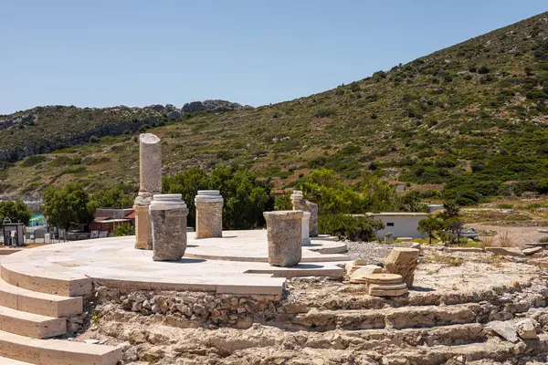 Türkiye 'de deniz manzaralı bir yamaçtaki antik kalıntılar. Taş yapılar ve sütunlar yeşil ve kayalık arazilerle çevrili olarak görülebilir..