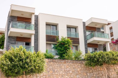 Balkonları ve yeşillikleri olan modern bir apartman. Yapıda, önünde çağdaş mimari sergilenen taş bir duvar ve yemyeşil bitkiler yer alıyor..