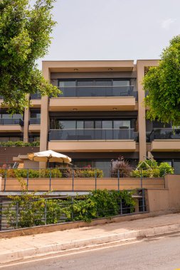 Geniş balkonları ve yeşillikleri olan modern bir apartman. Çağdaş bir tasarıma sahip olan yapı ağaçlar ve bitkilerle çevrilidir..