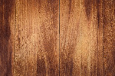 Tahta bir yüzeye yakın çekim. Kahverengi tonlar ve görünür tahıl desenleri var. Doku pürüzsüz ve cilalı, doğal ahşap özellikleri sergiliyor..