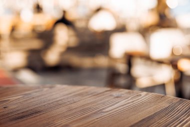 Ahşap bir masa yüzeyine yakın plan ve bulanık bir arka plan. Tahtanın zengin bir dokusu ve sıcak bir tonu var, rahat bir atmosfer yaratıyor..