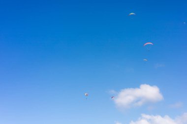 Renkli paraşütçüler bulutlarla dolu parlak bir gökyüzünde zarifçe süzülüyorlar. Arka planda beyaz bulutlar ile doğal mavi gökyüzü 
