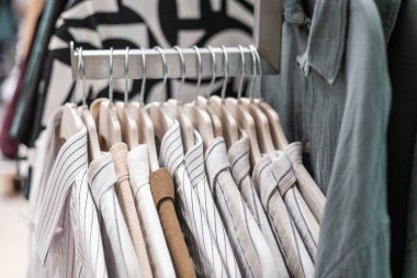 Perakende mağazasında düzgün düzenlenmiş çizgili ve katı gömlekler sergilenen bir askı. Gömlekler ahşap askılarda asılı, çeşitli renkler ve desenler sergileniyor..