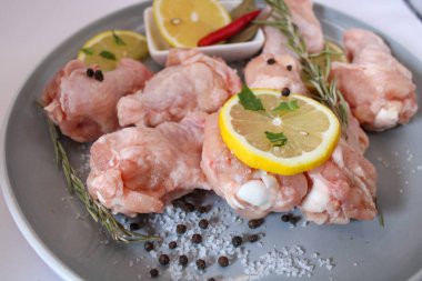 Gri bir tabakta baharat ve bitkilerle çiğ tavuk kanatları.