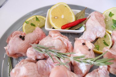 Gri bir tabakta baharat ve bitkilerle çiğ tavuk kanatları.