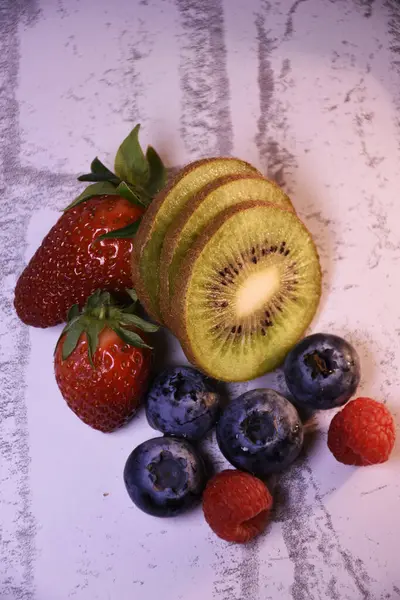 Gri arka planda meyveler ve meyveler, ahududu, yabanmersini, kivi, çilek.