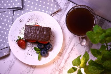 Beyaz bir tabakta taze böğürtlen ve nane çayı ile bir parça çikolatalı kek.