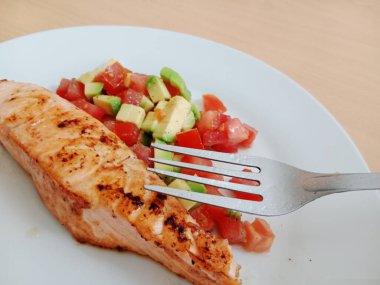 Sağlıklı kahvaltı, öğle yemeği, hafif akşam yemeği. Domatesli ızgara somon ve beyaz tabakta avacado salatası..