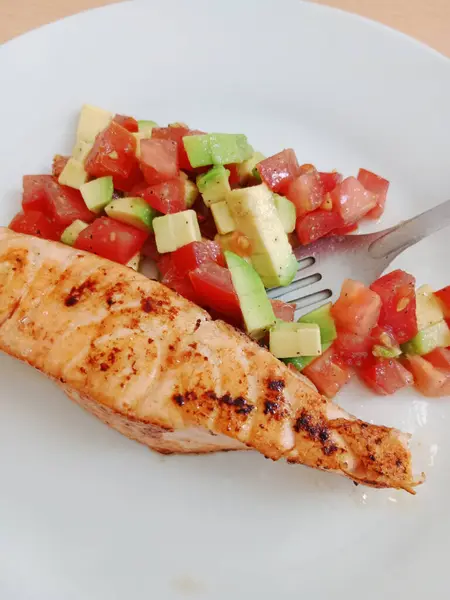 Healthy breakfast, lunch, light dinner. Grilled salmon with tomato and avacado salad on a white plate.