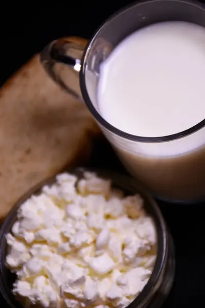 Ev yapımı peynirli bir fincan süt ve koyu arkaplanda bir parça ekmek.