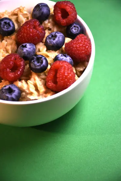 Yeşil zemin üzerinde taze yaban mersini ve ahududu bulunan lezzetli yulaf ezmesi.