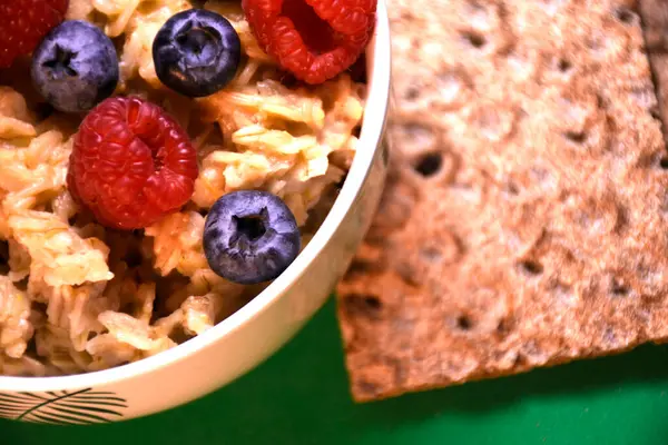 Yeşil zemin üzerinde taze yaban mersini ve ahududu bulunan lezzetli yulaf ezmesi ve tam tahıllı ekmek.