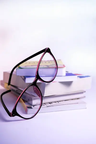 Masada kitap, gözlük ve kitap yığını var..