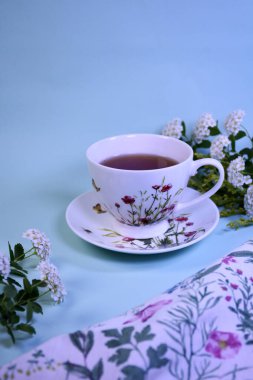 Mavi arka planda beyaz çiçekli aromalı çay tabağındaki porselen bardak.