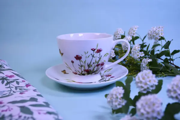 Mavi arka planda beyaz çiçekli aromalı çay tabağındaki porselen bardak.