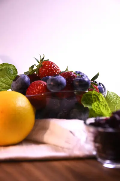 Beyaz arka planda cam bir kasede taze çilek ve yabanmersini..