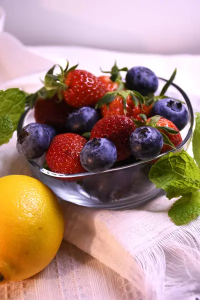 Beyaz arka planda cam bir kasede taze çilek ve yabanmersini..